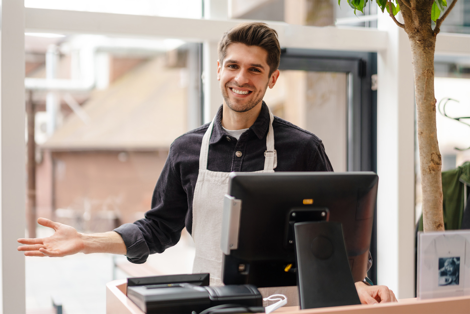 A cashier wearing an apron behind a counter with a computer on it